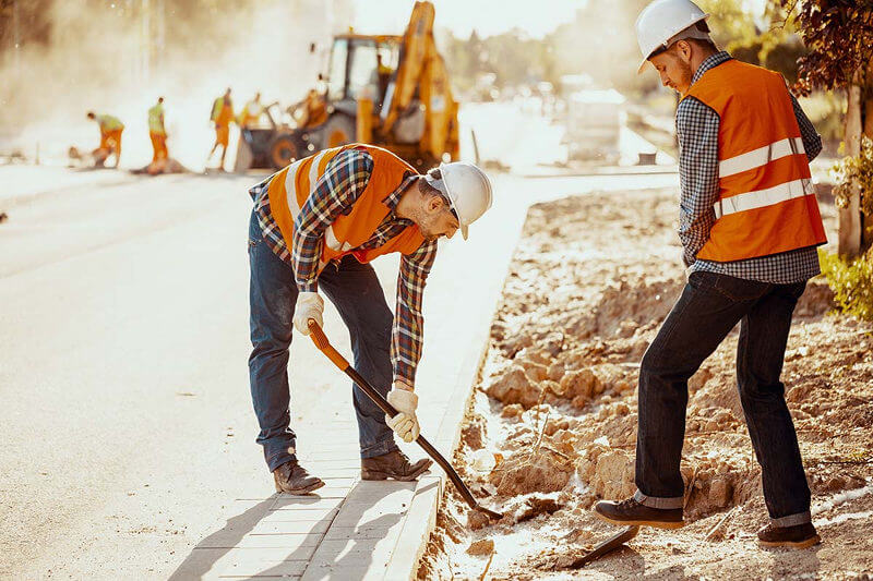 Two workings in orange vests digging on the side of the road